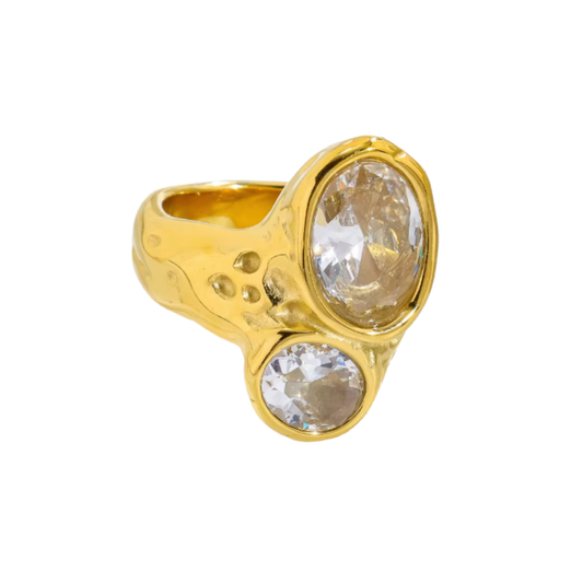 A gold ring featuring two large, bezel-set clear oval gemstones, one larger and one smaller, set in a textured, organic-shaped band.